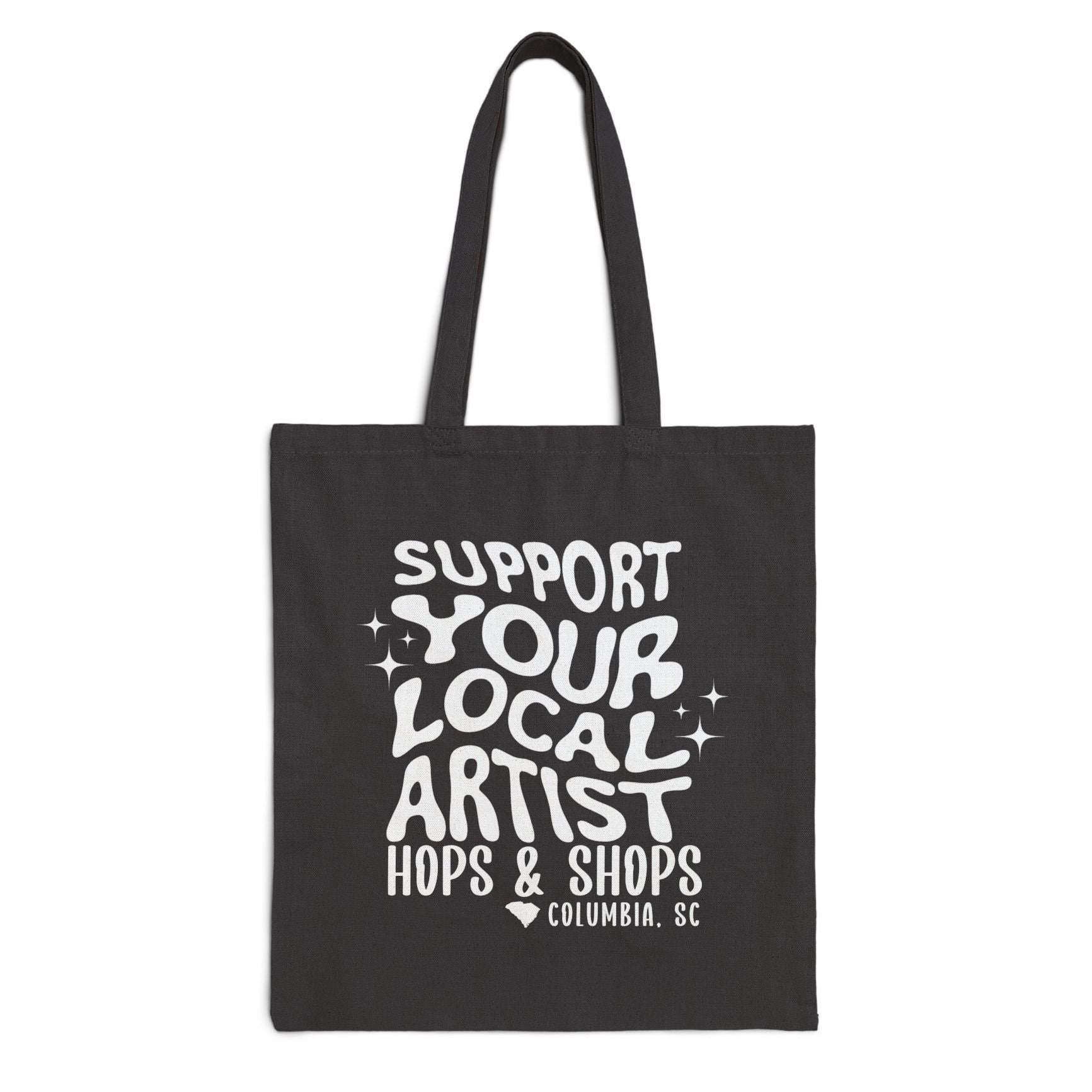 Black tote bag with white text 'Support Your Local Artist Hops & Shops Columbia, SC' on a white background